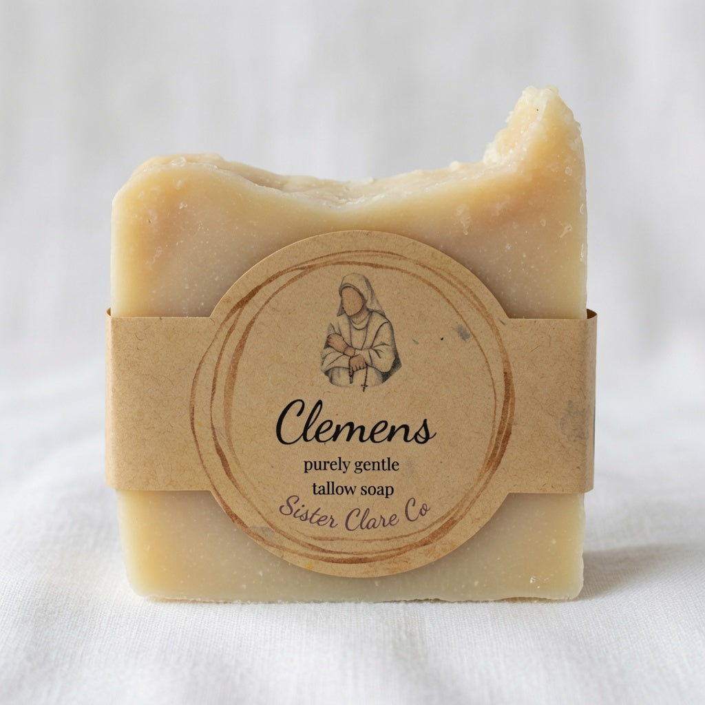 A single bar of Clemens tallow soap wrapped in a kraft paper band with a circular label reading 'Clemens' and 'Sister Clare Co', photographed against a soft white fabric background.