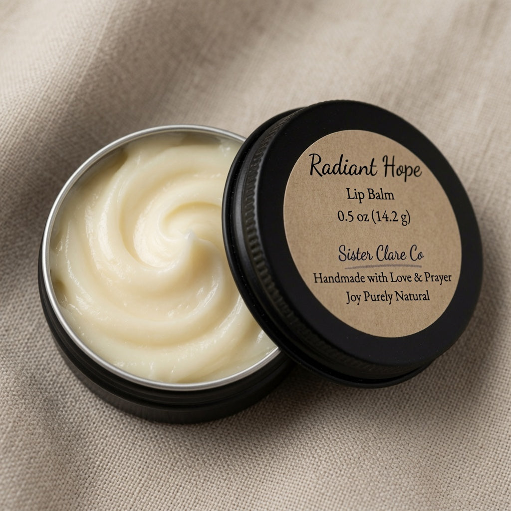 An open round black tin of lip balm with pale cream balm visible inside, next to a black lid labeled 'Radiant Hope Lip Balm' by Sister Clare Co, set on a beige fabric background.