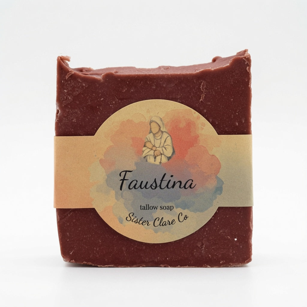 A rectangular bar of Sister Clare Co. Faustina tallow soap, wrapped in a beige paper band with a circular label featuring a watercolor illustration of a robed figure.