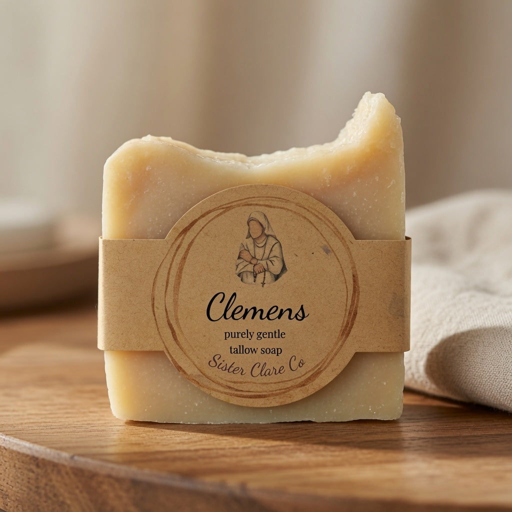 A rectangular bar of pale yellow soap wrapped in a kraft paper band with a round label reading 'Clemens' and 'Sister Clare Co,' placed on a wooden surface with a soft neutral background.