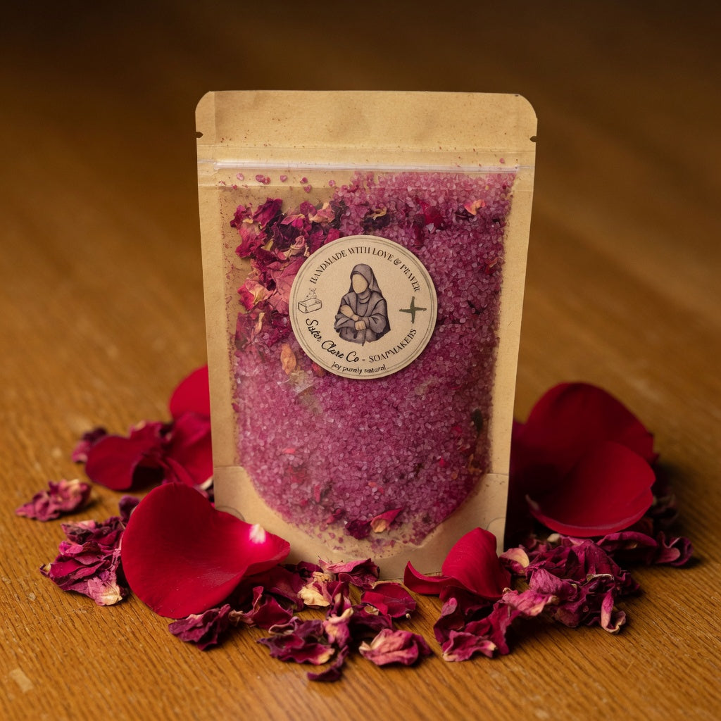 Themed square image of Lisieux Mineral Soak pouch surrounded by arranged rose petals on wood, creating an emotional, garden-like connection to St. Thérèse the Little Flower.