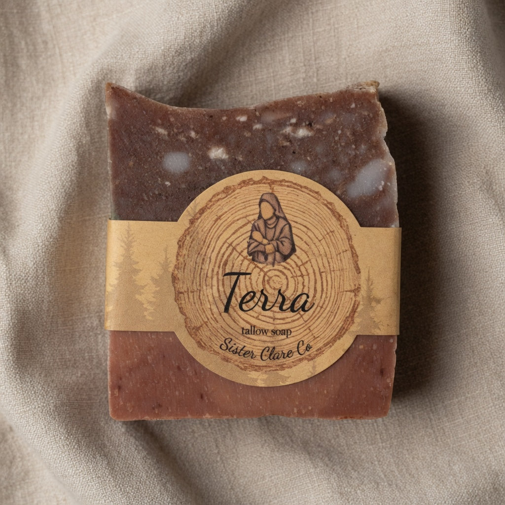 Close-up detail of Terra Tallow Soap on soft neutral linen fabric, emphasizing the marbled earthy texture, layers, and Sister Clare Co. circular nun logo label for clean product focus.